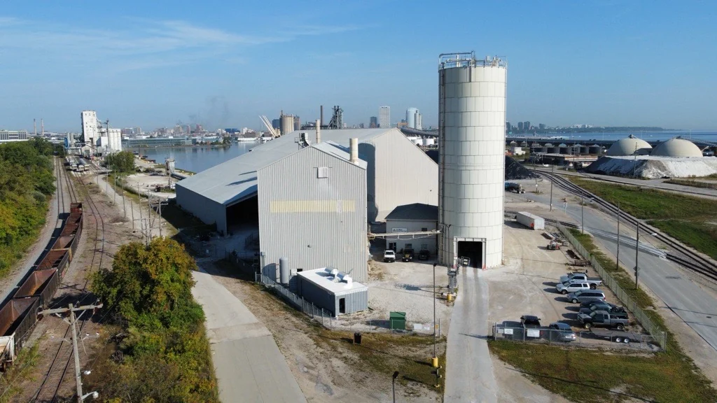 Aerial view of the Badger plant beside a rail line, with the Milwaukee skyline and Lake Michigan behind it